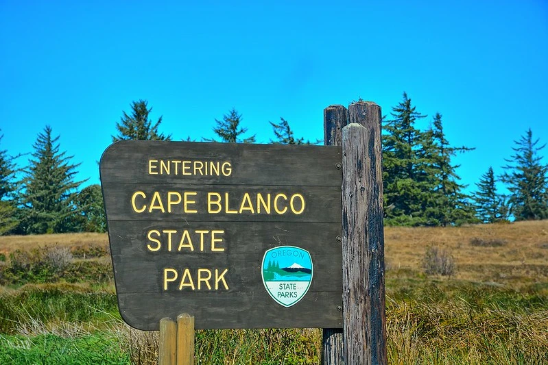 Park entrance sign for Cape Blanco State Park with lighthouse visible on the horizon